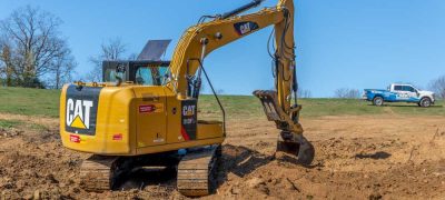 A yellow excavator with a large bucket arm and treads, scooping up dirt at a construction site.