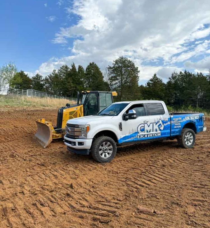 A construction site with a white pick-up truck of CMK Excavation and a yellow mini bulldozer.