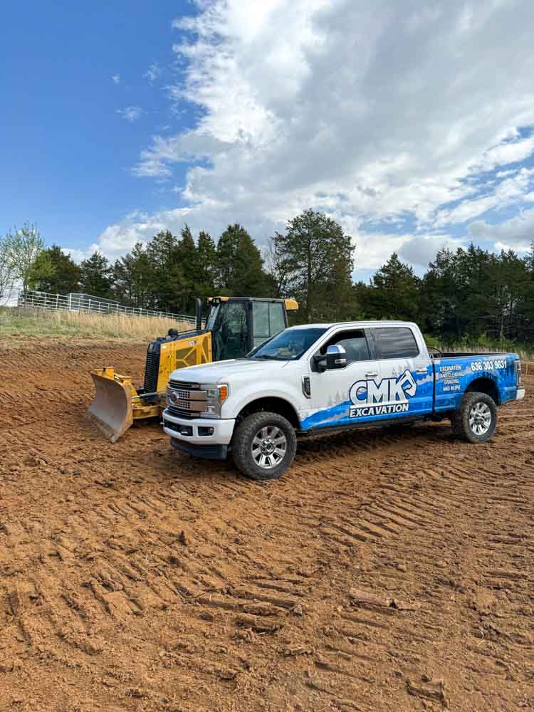 A construction site with a white pick-up truck of CMK Excavation and a yellow mini bulldozer.